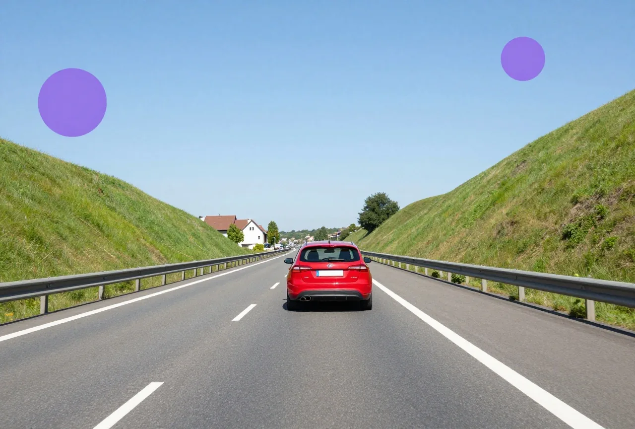 Ein rotes Auto fährt auf einer breiten Autobahn zwischen grünen Hügeln unter blauem Himmel